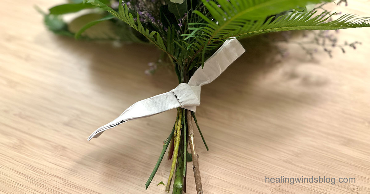 紫陽花のスワッグの茎元に願い事を書いた半紙が巻きつけられ、しっかりと結ばれている様子。手書きの願いをそっと包み込み、お守りのように仕立てられている。